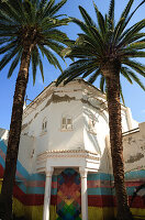  Street photography in Rabat, Morocco, showing a white house next to some palm trees painted with colorful graffiti. 