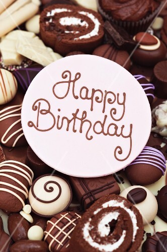 Happy Birthday lettering on a disc of icing, on top of chocolate cakes and sweets