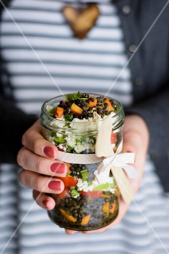 A woman holding a glass jar of lentil salad in her hands