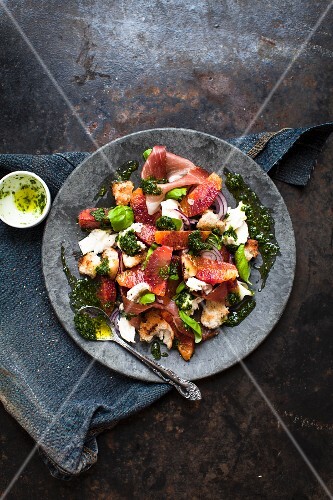 A salad with prosciutto, mozzarella, pesto, blood orange and bread