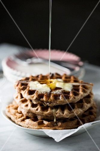 Syrup being poured onto a stack of waffles
